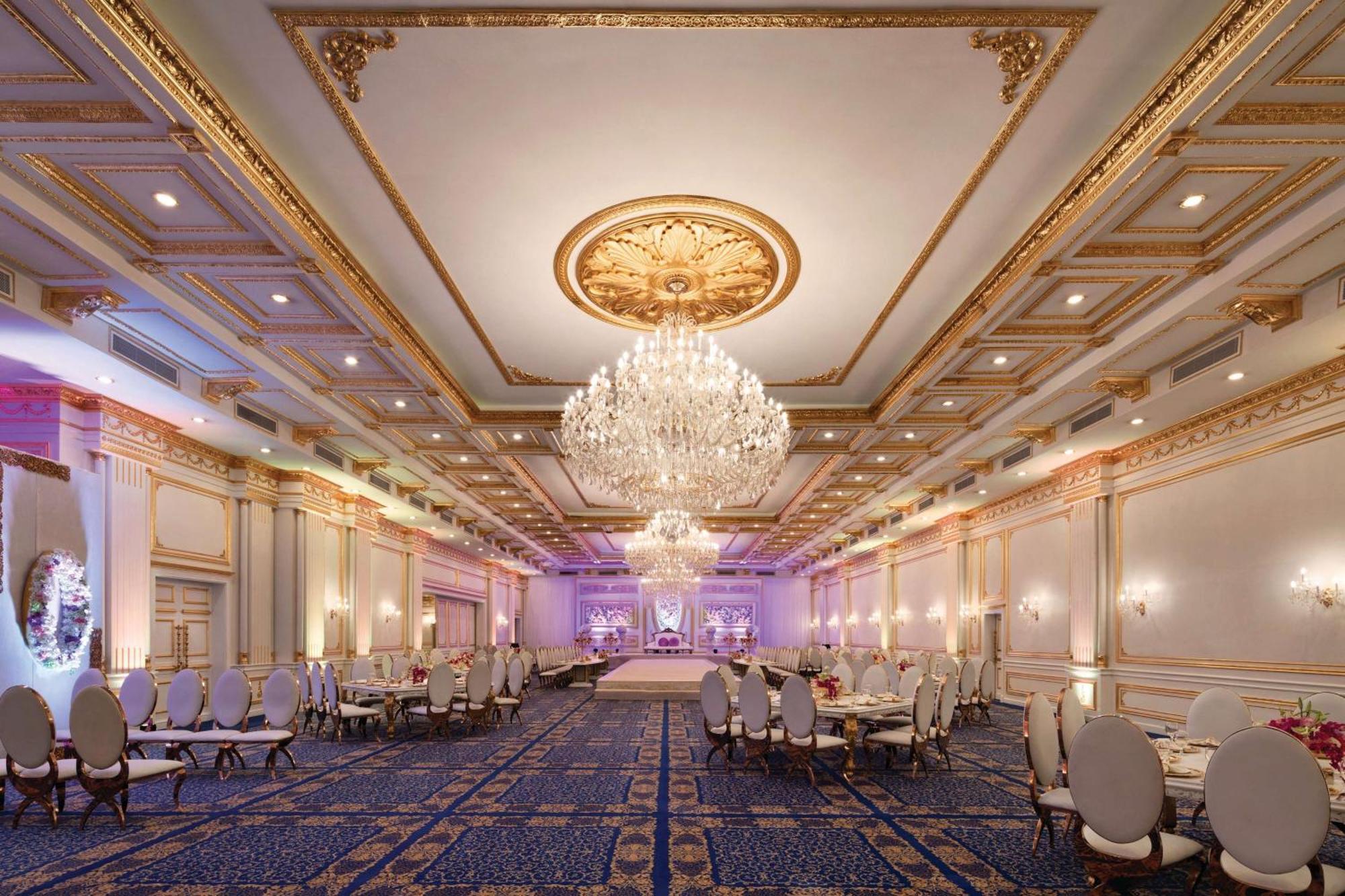 Grand Regency Doha, Trademark Collection By Wyndham Exterior photo The photo shows an elegant banquet hall with luxurious decor. The room features high ceilings adorned with intricate gold details and a large chandelier that hangs in the center, providing soft illumination. There are several round tables with plush 