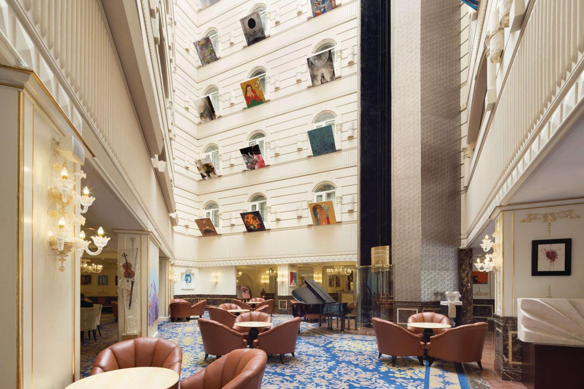 Grand Regency Doha, Trademark Collection By Wyndham Exterior photo The photo depicts the interior of a spacious, upscale hotel lobby. The design features high ceilings and multiple levels, with large windows that create a bright and airy atmosphere. Elegant light fixtures adorn the walls, and the floor is covered wi