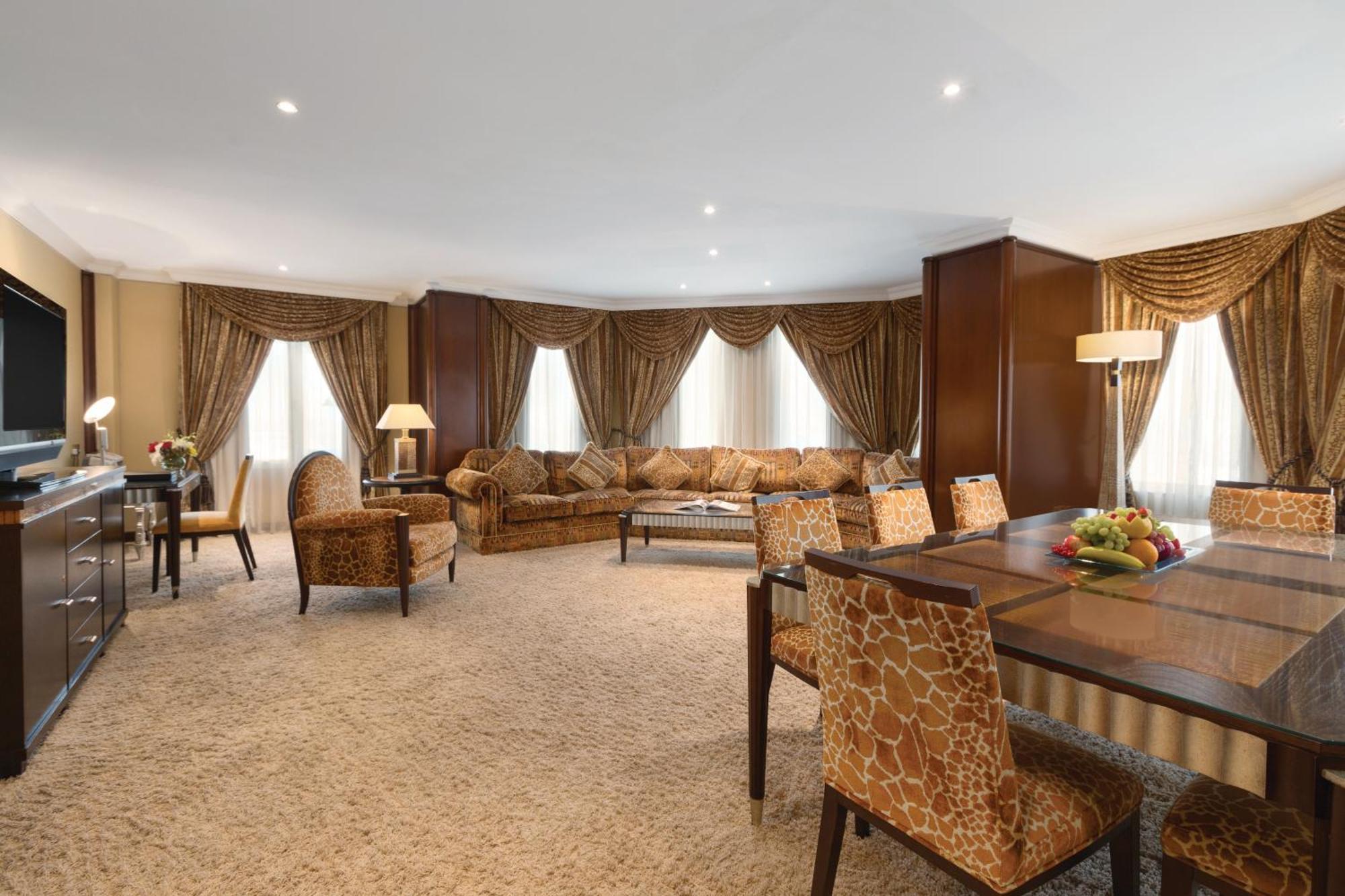Grand Regency Doha, Trademark Collection By Wyndham Exterior photo The photo shows a spacious and elegantly designed living area. There are large windows dressed with luxurious curtains, allowing natural light to fill the room. The seating arrangement features a comfortable sofa with various cushions and several sty
