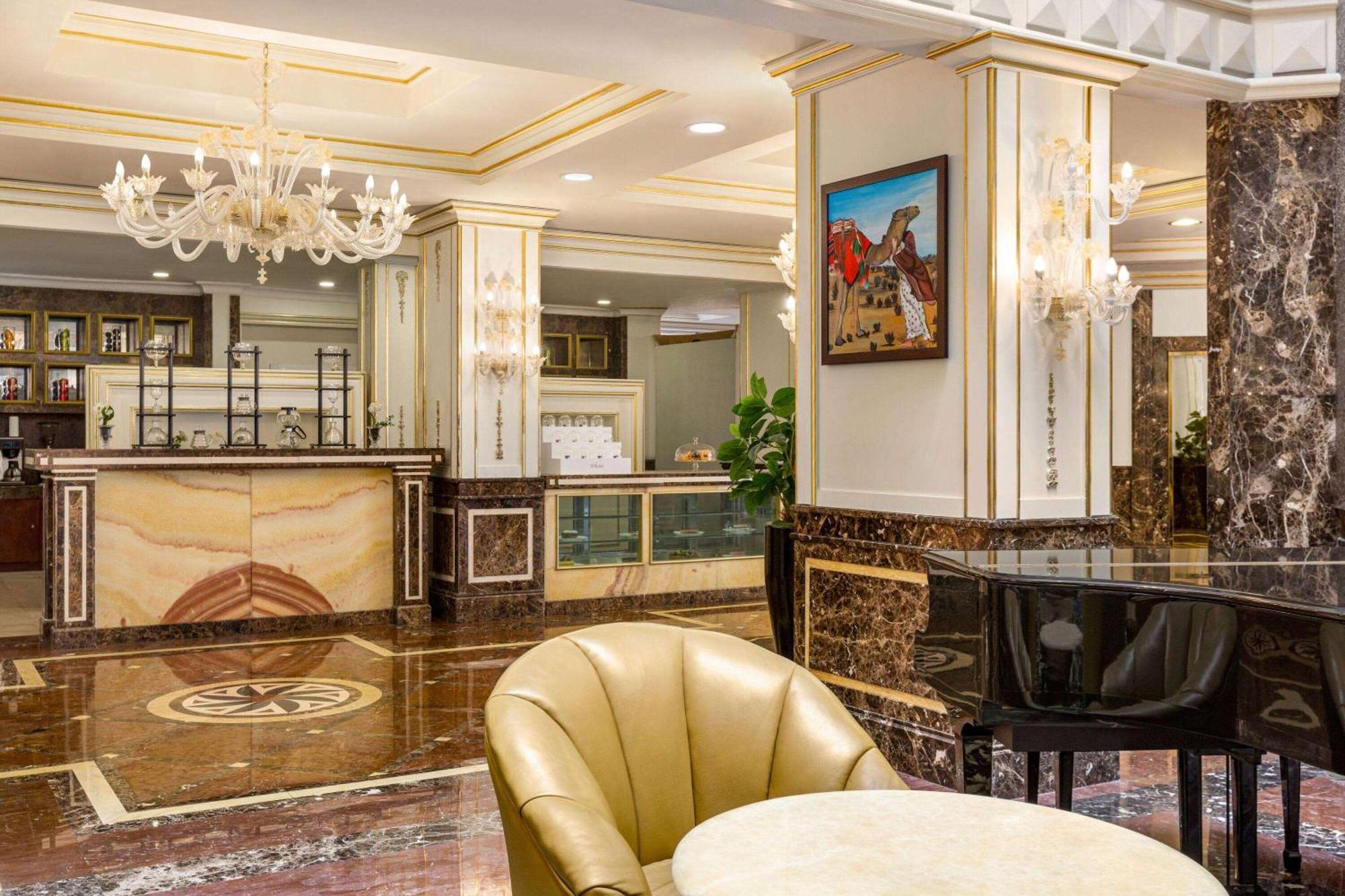 Grand Regency Doha, Trademark Collection By Wyndham Exterior photo The photo depicts an elegant hotel lobby interior. It features a polished marble floor with intricate patterns. In the background, there is a reception desk made of marble and wood, with decorative elements and a glass display. On the walls, you can 