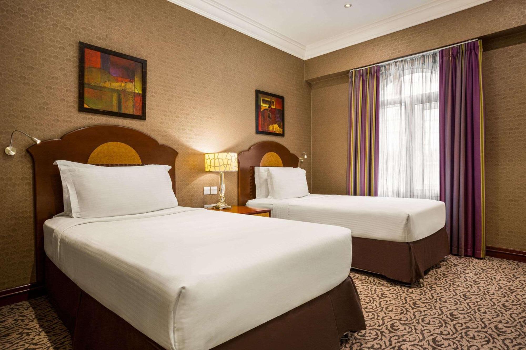 Grand Regency Doha, Trademark Collection By Wyndham Exterior photo The photo shows a hotel room featuring two single beds with white bedding and dark brown upholstered headboards. There is a bedside table with a lamp between the beds. On the walls are two abstract paintings, and large windows dressed with sheer curt